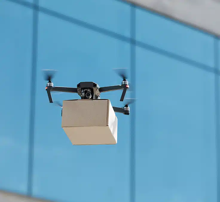 Foto de un drone de color negro volando y portando un paquete